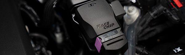 RaceChip S control unit close-up in an engine bay, black housing with RaceChip logo, product label and purple OEM connector.